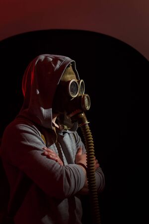 Human in gas mask in red light rays standing sideways on black background. Enviromental protection, radiation ans biohazard concept.の写真素材