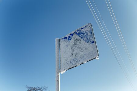Traffic sign covered with snow on blue sky background at winter sunny dayの写真素材