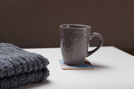 Cup of hot coffee or cacao and grey knitted scarf near on white table background. Cozy autumn or winter, hot drinks, homemade beverages concept.の写真素材