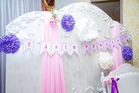 Beautiful tender white photo zone with inscription on paper flags - Happy birthday. Pink curtains and purple paper flowers. Birthday party decorative elements for a girl.の写真素材