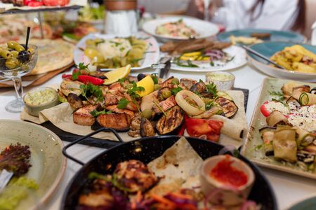 Festive dishes with grilled meat and vegetables, tomato, lemon, vegetable salads, olives decorated with parsley. Wedding or birthday table setting. Banquet in restaurant or cafe.の写真素材