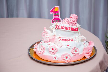Girlish cake with pink mastic flowers and cnumber 1. One year old first birthday party. Inscription on candle My birthday. Inscription on cake - name Ksushenka is one year old.の写真素材