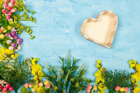 Artificial multicolored flowers and wooden empty heart shaped box on blue painted wooden background. Spring blossom, Easter, women day, mothers day, 8 March concept. Copy space.の写真素材