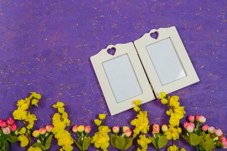 Artificial yellow and pink flowers and empty white frame or mock up on purple painted wooden background. Spring blossom, Easter, women day, mothers day, 8 March concept. Copy space.の写真素材