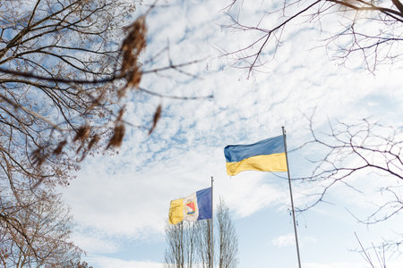 Ukrainian yellow and blue flag and coat of arms of Ukrainian town Izmail flying on blue cloudy sky...