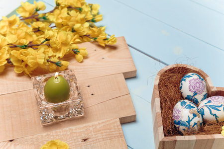 Heart shaped box with decorated Easter eggs, yellow flowers, burning candle and brown boards on...