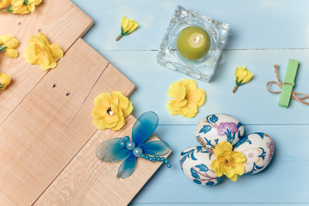 Decorated Easter eggs, yellow flowers, burning candle on wooden blue boards background. Spring and...