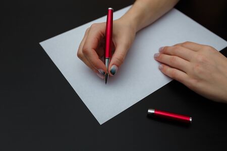 Female hands with fir-tree forest manicure holding red pen over white paper on black background. Christmas or winter nail art. Hands care, fingernails design, beauty and health concept. Copy space.の写真素材