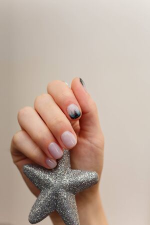 Female hands with fir-tree forest manicure holding silver toy star on white background. Christmas or winter nail art. Hands care, fingernails design, beauty and health concept. Copy space.の写真素材