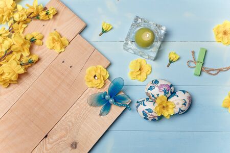 Decorated Easter eggs, yellow flowers, burning candle on wooden blue boards background. Spring and Easter concept. Copy space.の写真素材