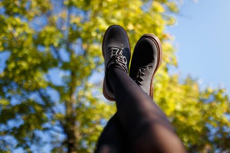 Female feet in grey shoes lifted up to blue sky and green trees background, low angle view. Relaxation, fun concept.の写真素材