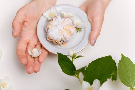 female hands holding plate with sugar powdered cake and some jasmine flowers on white table.の写真素材