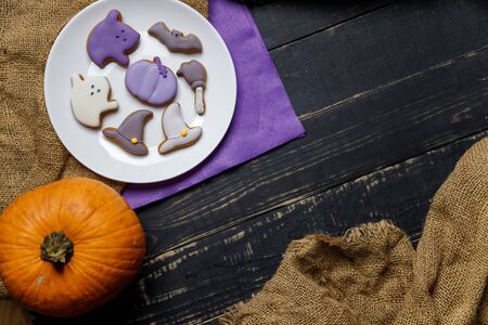 Pumpkin and Halloween cookies on white plate, sackcloth on black wooden background. Hallooween trick or treat concept. Copy space.の写真素材