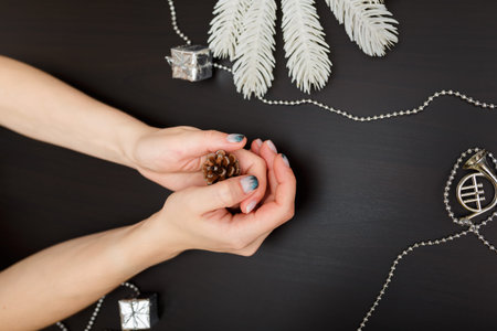Female hands with fir-tree forest manicure holding pine cone on black background. Christmas or...