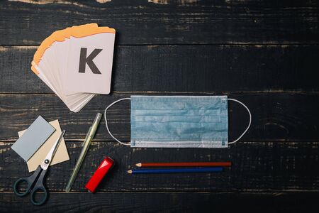 Alphabet letters cards, stickers, scissors, pencils and medical gauze mask on wooden table. Coronavirus infection Covid 2019 outbreak, selfisolation, distant learning, home education, remote study concept. Copy space.の写真素材