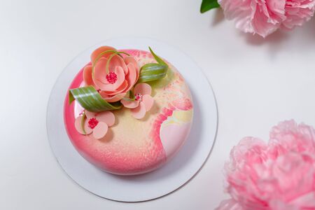 Soft focused shot of mirror glaze birthday cake with pink flowers and peony on white background. Sweet festive pastry for girl or woman. Place for text.の写真素材