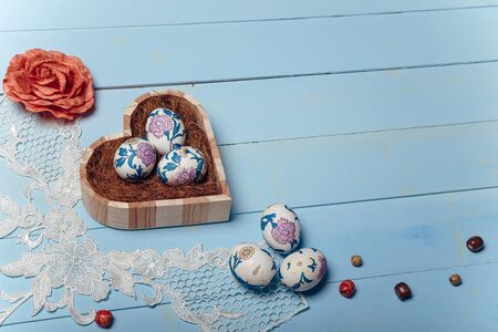 lose up shot of Easter eggs in wooden heart shaped box with decorative elements on blue background. Easter and spring concept. Top view, copy space.の写真素材
