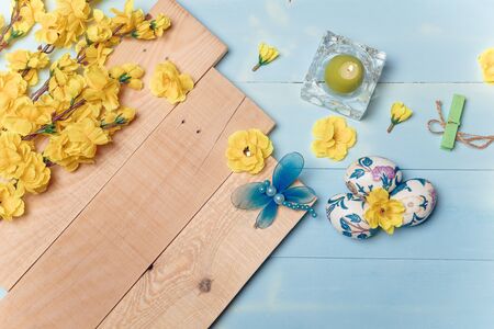 Decorated Easter eggs, yellow flowers, burning candle on wooden blue boards background. Spring and Easter concept. Copy space.の写真素材