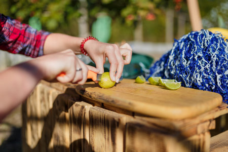 Hands slicing fresh lime on wooden cutting board for outdoor party coctails or beverages. Summer...