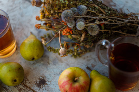 Dry healing herbs bouquet, cup of herbal tea and some fresh fruits, apples and pears on rustic background.の写真素材