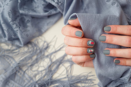 Female hands with Merry Christmas reindeer manicure on finger nails holding grey shawl. New Year,...