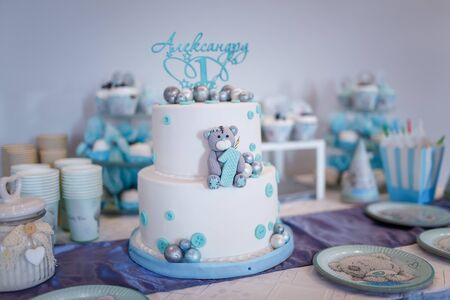 Izmail, Ukraine - July 2019. Editorial use. Birthday cake for a one year old boy. Teddy bear cartoon character shape and blue decorations of mastic. Candy bar. Inscription Alexandr is 1 year.の写真素材
