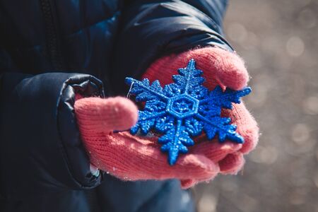 Child hands in mittens holding blue shiny snowflake toyの写真素材