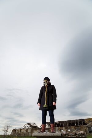 Human in gas mask standing among ruins and dramatic sky background. Enviromental pollution, ecology disaster, radiation, biological hazard concept.の写真素材
