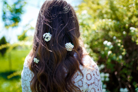 Girl standing back to camera with white spirea flowers in dark long wavy hair. Spring blossoming and...
