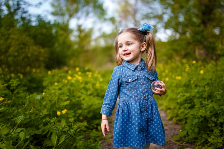 Funny little girl with two ponytails in blue dress among blooming yellow flowers of celandine. Springtime blossom and carefree childhood concept.の写真素材