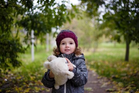 Little girl iwalking in autumn park and holding soft sheep toyの写真素材