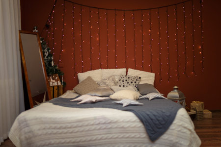 Modern bedroom interior with bed and cushions, toys and garland on the brown wall background. Merry...