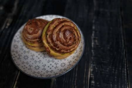 Two cheese and dill bread buns on plate standing on black wooden background. Tasty unhealthy food. Diet, nutrition, eating habits concept. Place for text.の写真素材