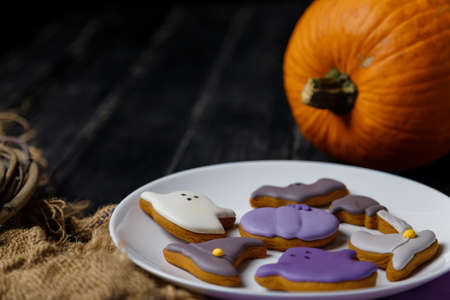 Pumpkin and Halloween cookies on white plate, sackcloth on black wooden background. Hallooween trick or treat concept. Copy space.の写真素材