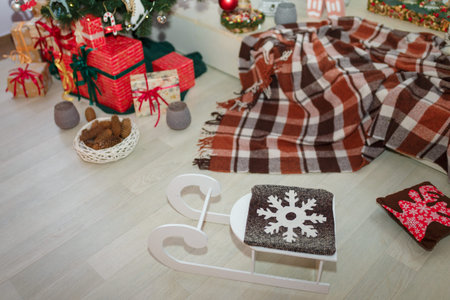 White wooden decorative sledge, pillows with snowflake and reindeer, decorated fir-tree with gifts...