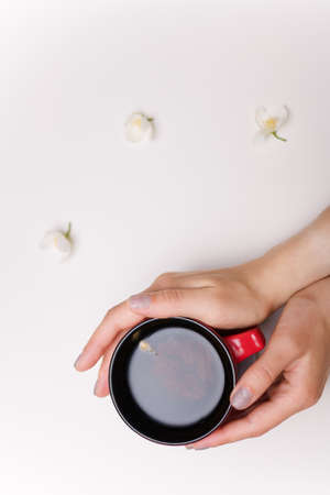 Female hand holding cup of jasmine tea. Some flowers on white table background. Healthy drinks, spring blossom concept. Top view, copy space.の写真素材