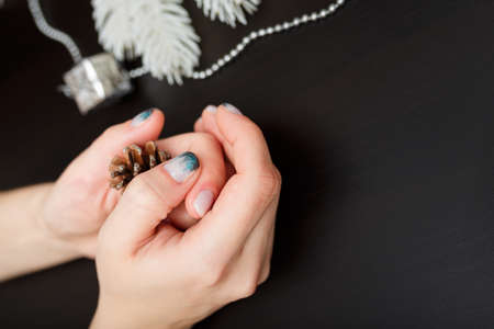 Female hands with fir-tree forest manicure holding pine cone on black background. Christmas or winter nail art. Hands care, fingernails design, beauty and health concept. Copy space.の写真素材