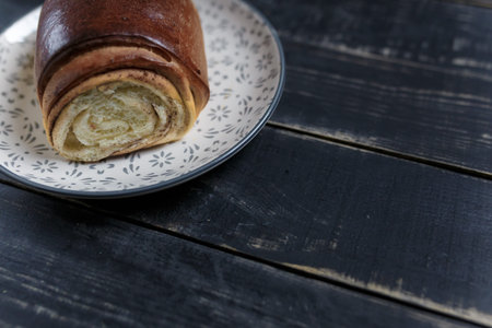 Cinnamon bread bun on plate standing on black wooden background. Tasty food, snack for breakfast or...