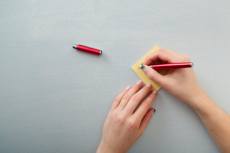 Female hands with fir-tree forest manicure holding red pen over yellow paper stickers. Christmas or...