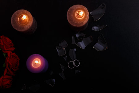 Love triangle and broken relationship concept. Wedding rings and three burning candles on black...
