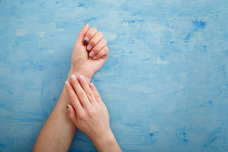Female hands with fir-tree forest manicure on blue background. Christmas or winter nail art. Hands care, fingernails design, beauty and health concept. Copy space.の写真素材