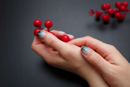 Female hands with fir-tree forest manicure holding red berries on black background. Christmas or winter nail art. Hands care, fingernails design, beauty and health concept. Copy space.の写真素材