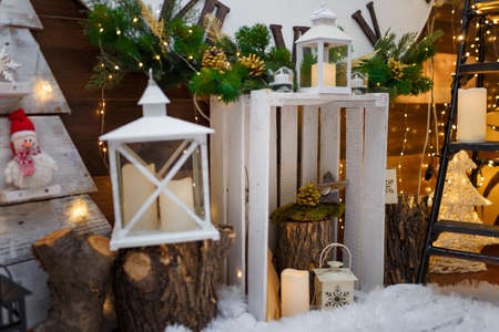 Merry Christmas and Happy New Year decorations standing on artificial snow. White wooden box, lanterns, candles, wooden toys, fir tree branches and warm garland lights. Winter holidays concept.の写真素材