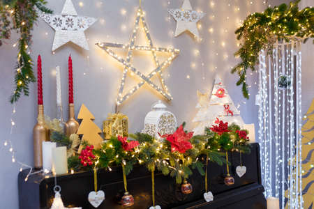 Merry Christmas, Happy New Year decorations with shiny stars, candles, white lantern, fir branches, bulbs, wooden toy hearts and warm garland lights over a fireplace or piano. Winter holiday concept.の写真素材