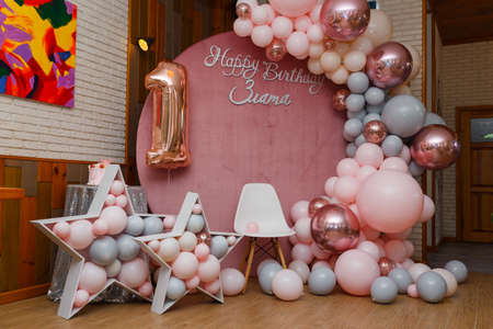 Beautiful festive decorations, pink and gray balloons arch, wooden stars, white chair and number one balloon on wooden round background. Little 1 year old girl birthday party photo zone.の写真素材