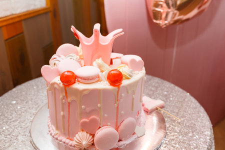 Tender pink cake with hearts, macaroons and princess crown on shiny silver table cloth. Festive...