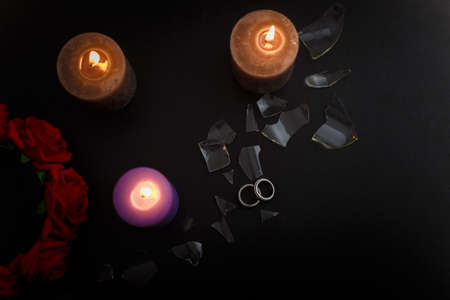 Love triangle and broken relationship concept. Wedding rings and three burning candles on black background. Flat lay, top view, place for text.の写真素材