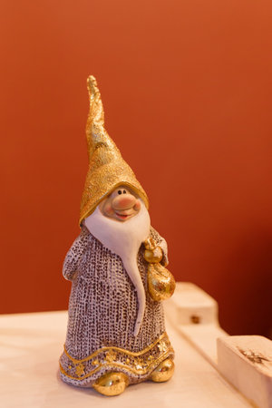 White and golden Santa Claus toy on white shelf on brown background. Winter holidays, Merry...