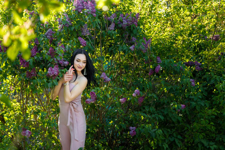 Beautiful dark-haired model posing among blossoming lilac bushes on spring background.の写真素材