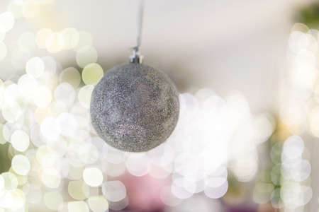 Silver bauble hanging on unfocused background with shiny sparkling garland lights and bokeh. Christmas tree toys and New Year decorations. Winter holidays miracle. Copy space.の写真素材